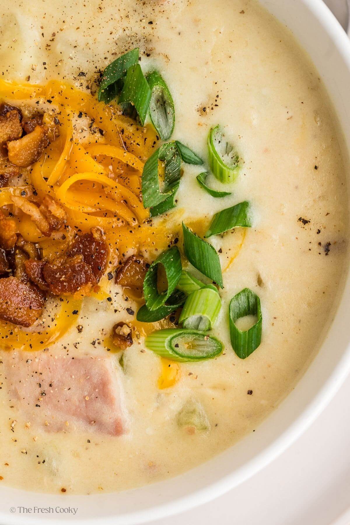 Overhead view of a bowl of ham and potato soup topped with bacon, cheese and green onions.