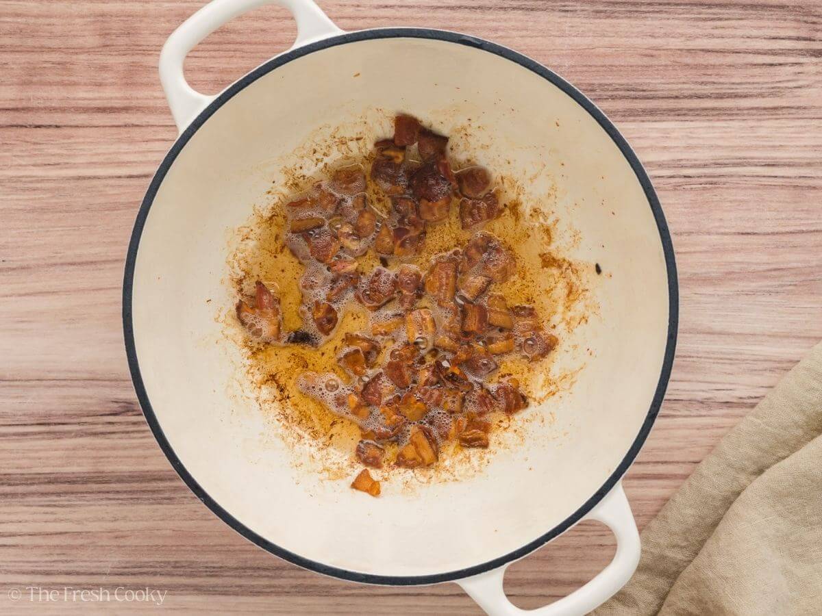 Pieces of bacon sizzling in the bottom of a large stock pot.