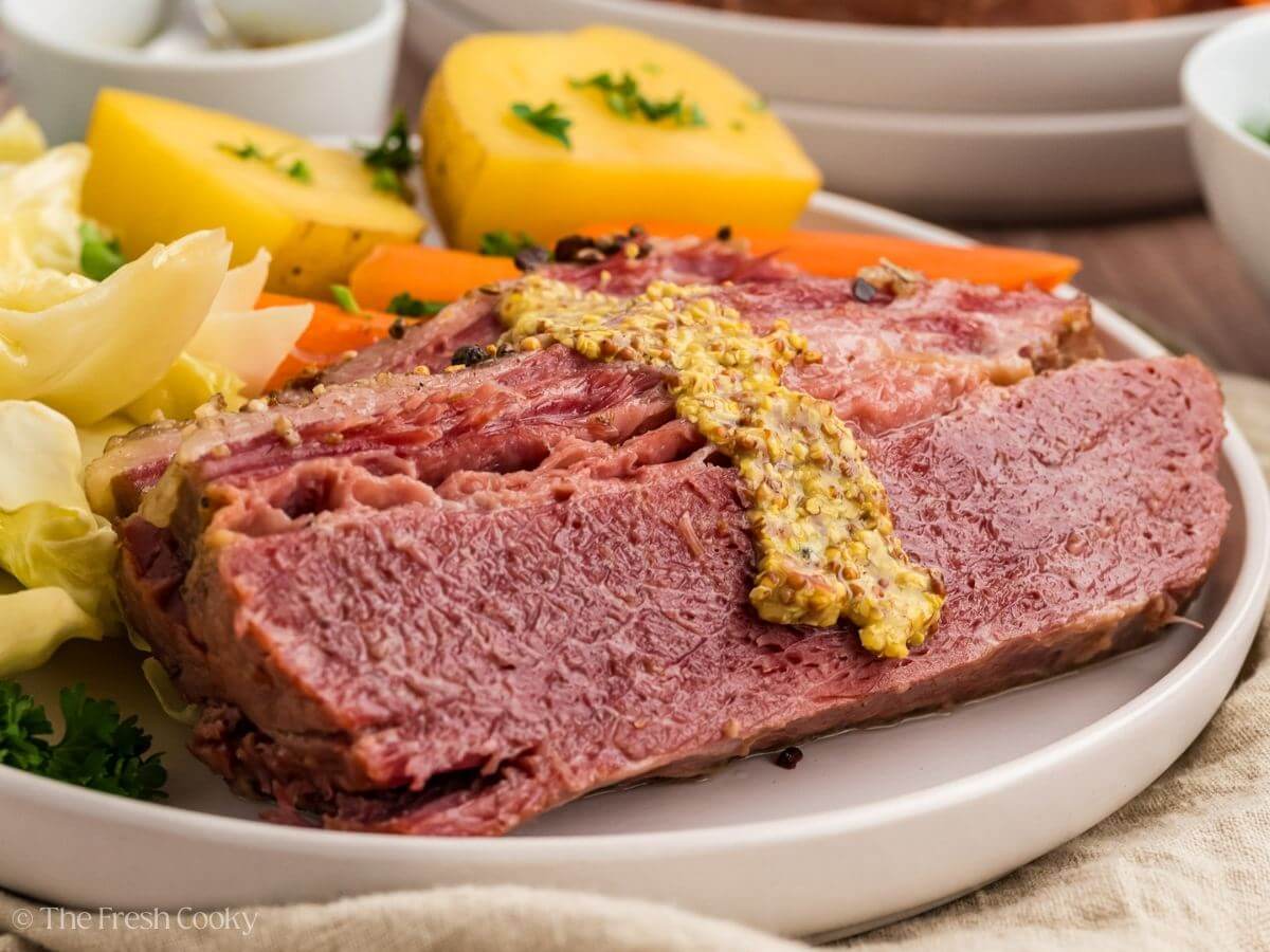 Crock pot corned beef on a plate with whole grain mustard, potatoes, carrots and cabbage.