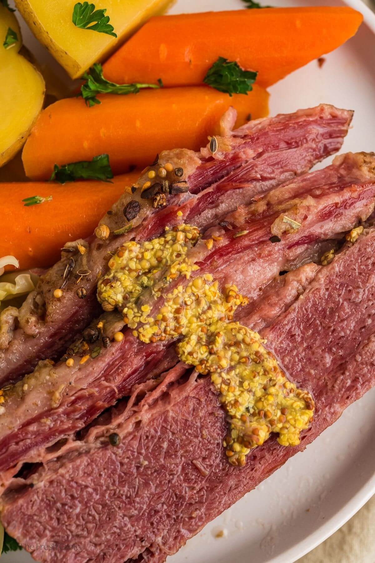 Close up of slices of corned beef on a plate topped with whole grain mustard.