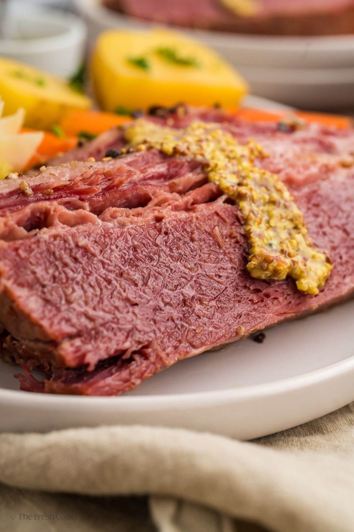 Side view of sliced corn beef on a plate topped with whole grain mustard.
