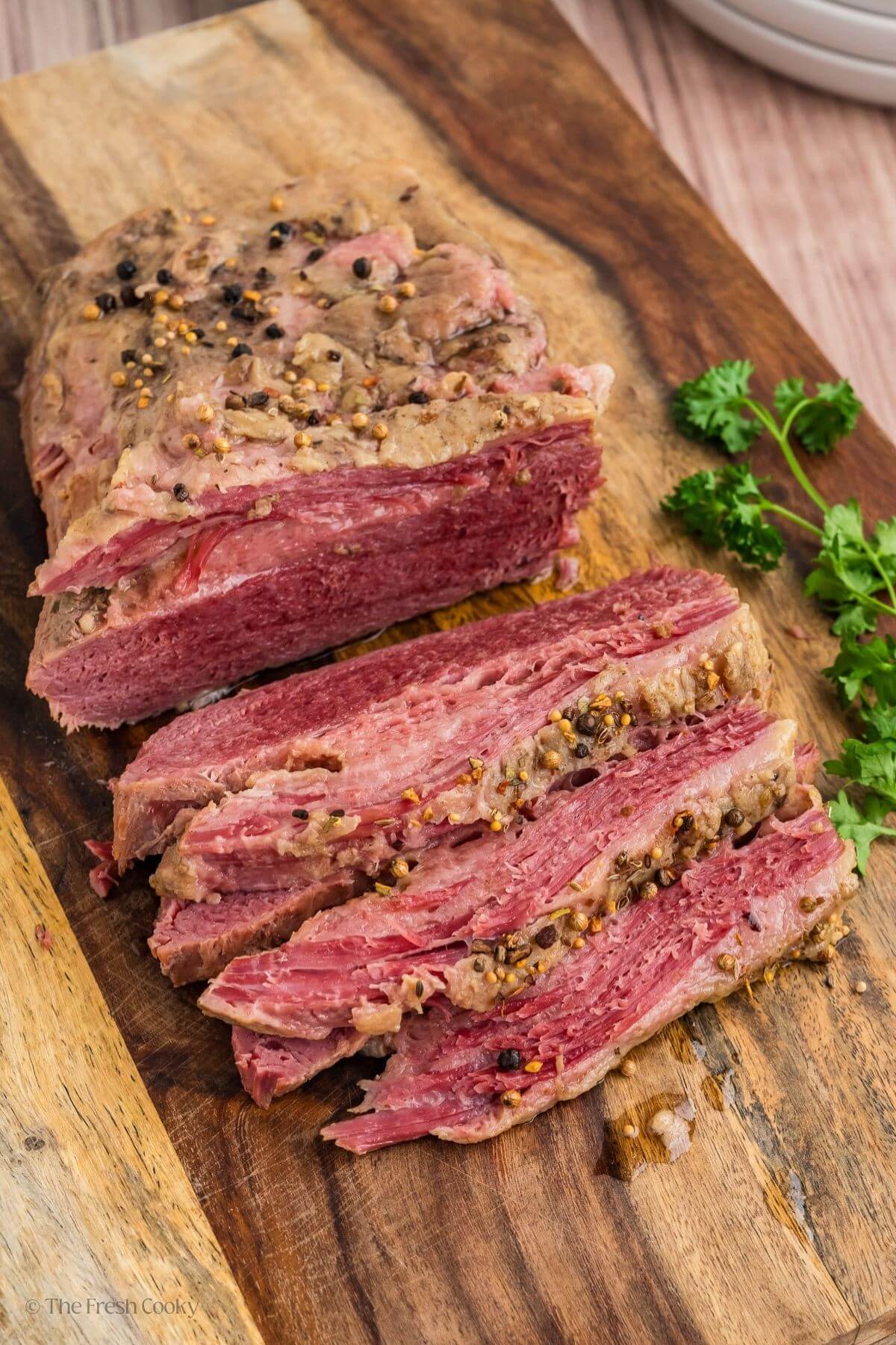 Corned beef brisket on a wooden board with some slices off the end.