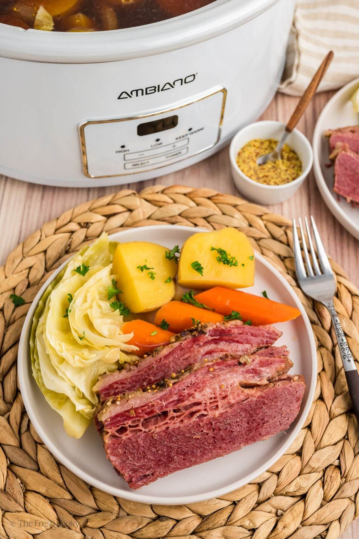 Plate served with corned beef, cabbage, carrots and potatoes next to a crock pot.