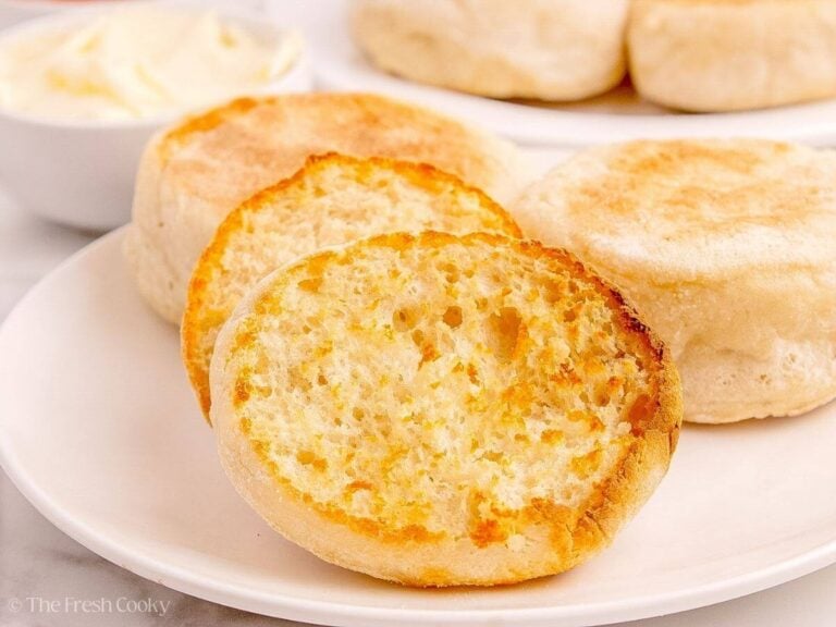 Crispy toasted sourdough English muffins on a plate with one of them cut in half.