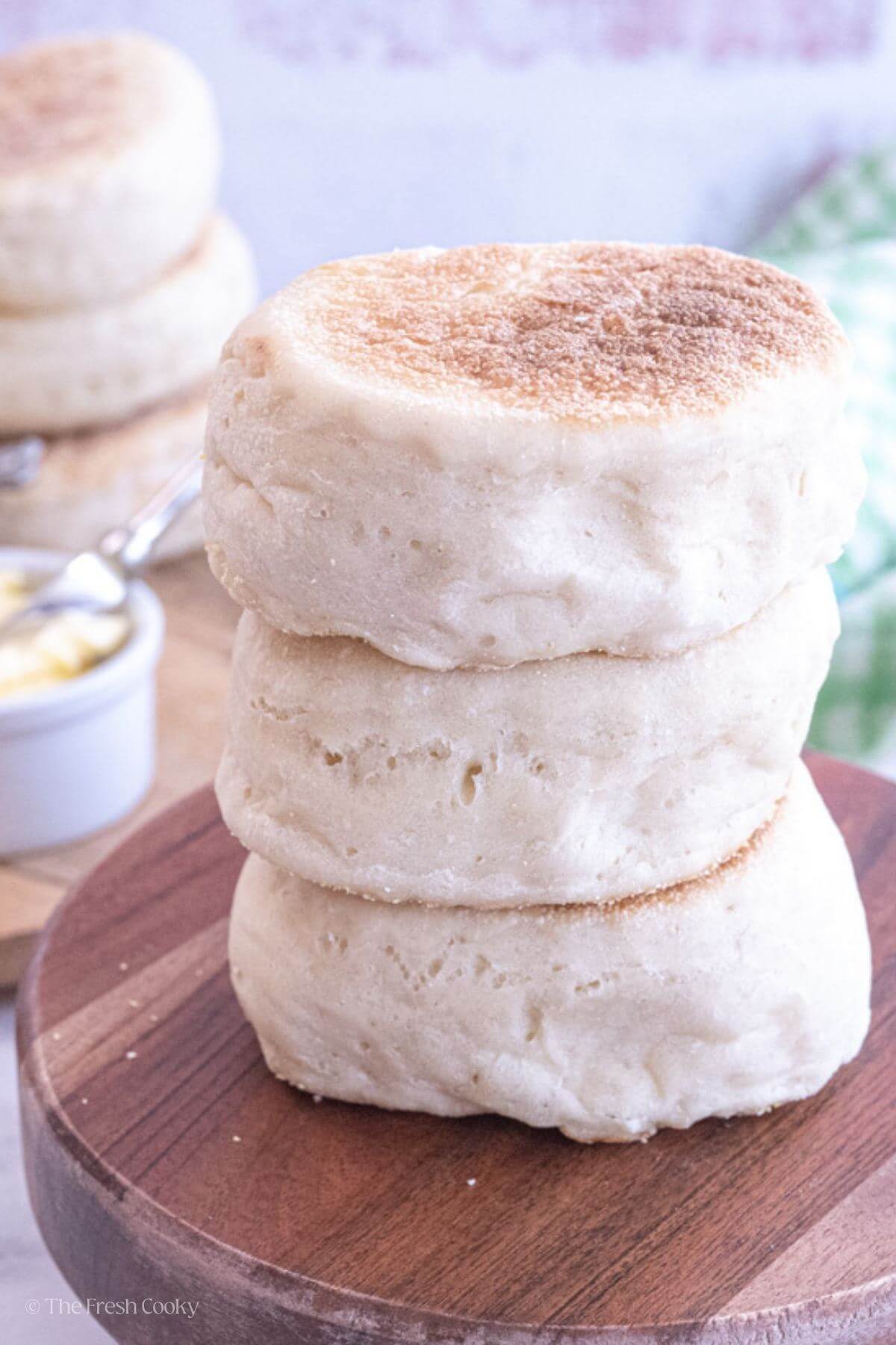 Three fluffy English muffins stacked on top of each other on a wooden board.