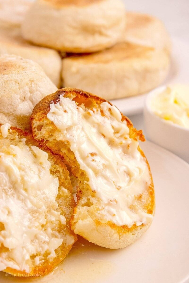 Toasted English muffin slathered with butter, missing a bite, and leaning against more English muffins.