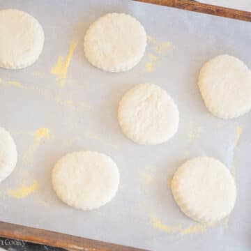 Unbaked English muffins on a sheet pan lined with parchment paper.