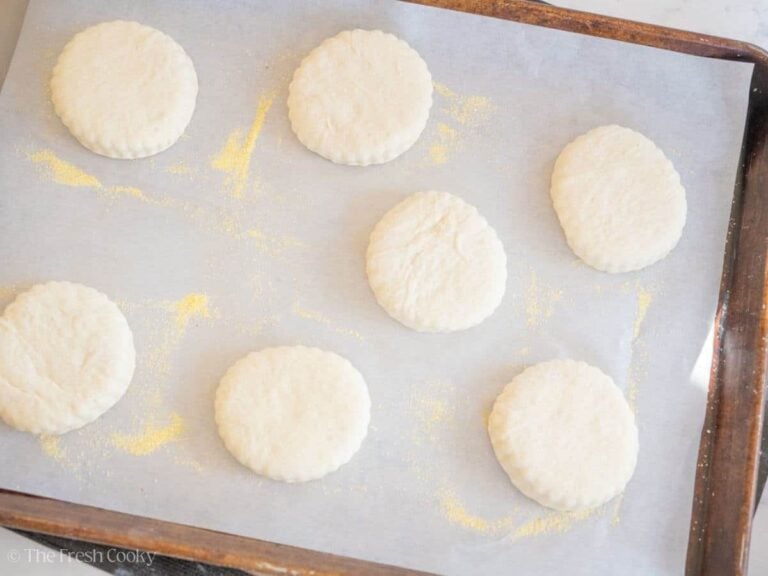Unbaked English muffins on a sheet pan lined with parchment paper.