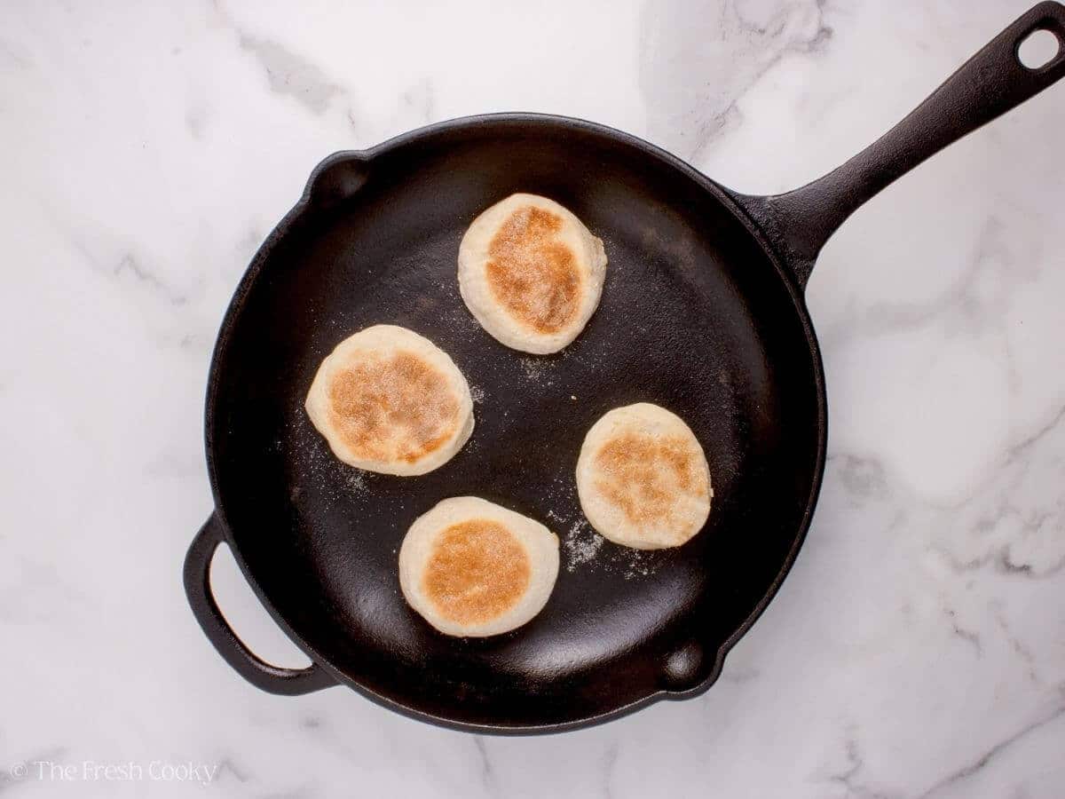 English muffins in a skillet after being flipped.