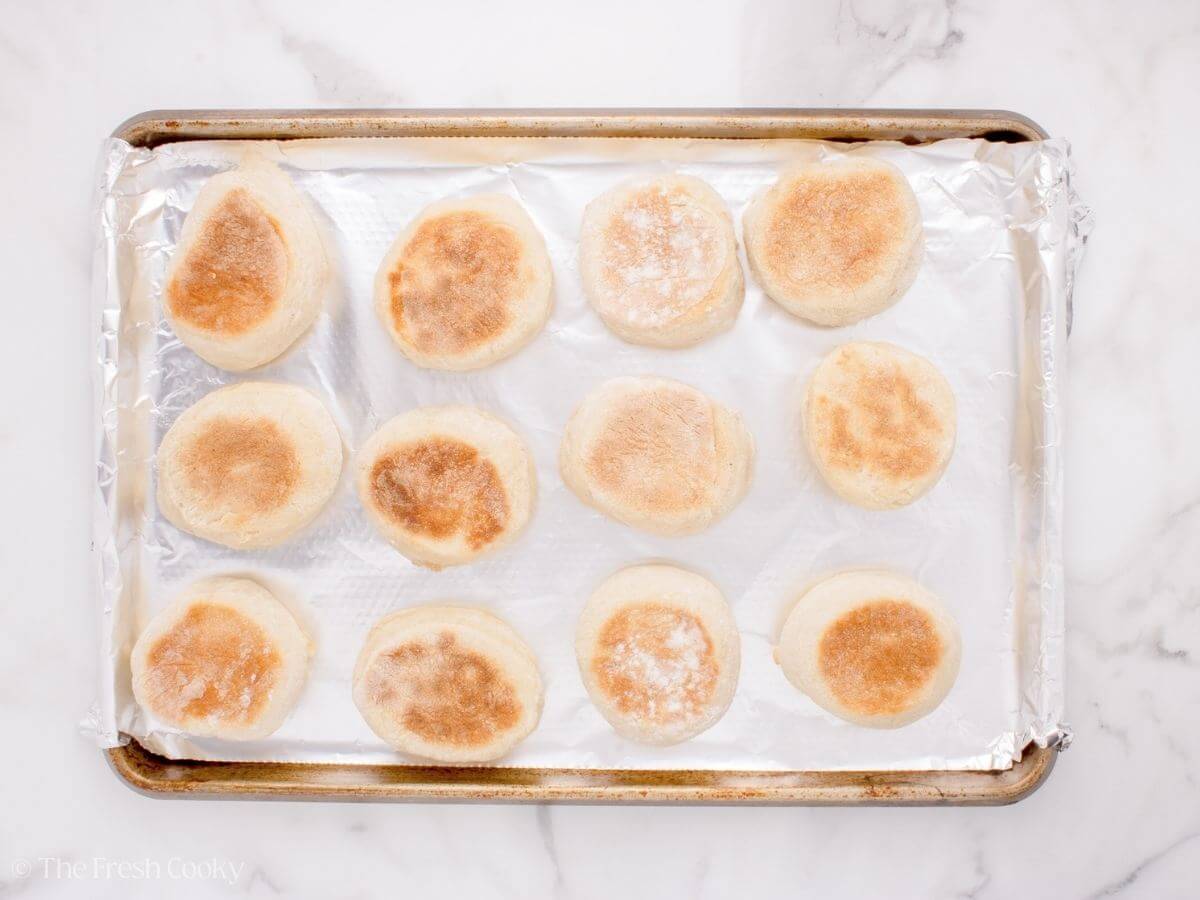 Seared English muffins on a sheet pan.