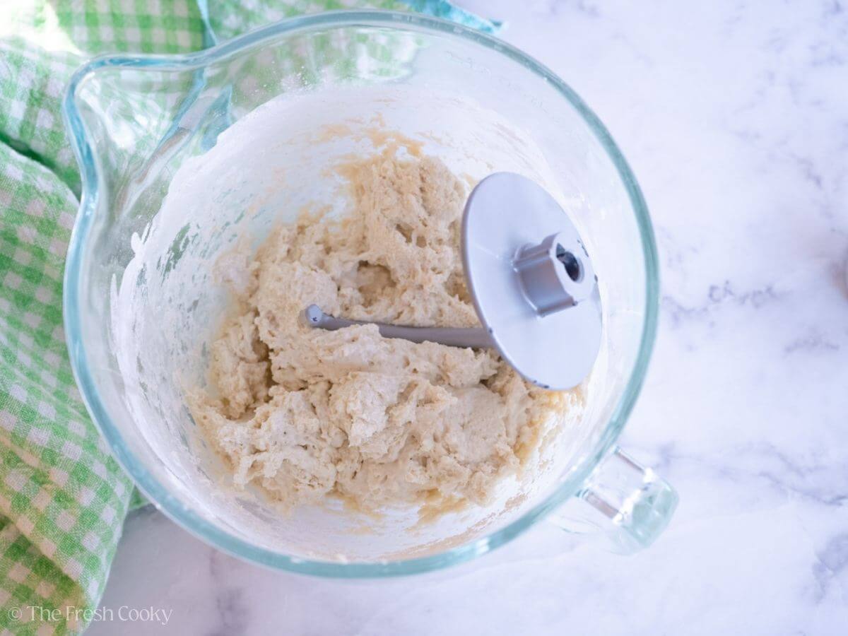 English muffin dough in a stand mixer with a dough hook.