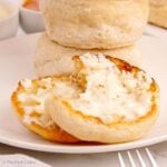 Two halves of a sourdough discard English muffin slathered in butter with more in the background.