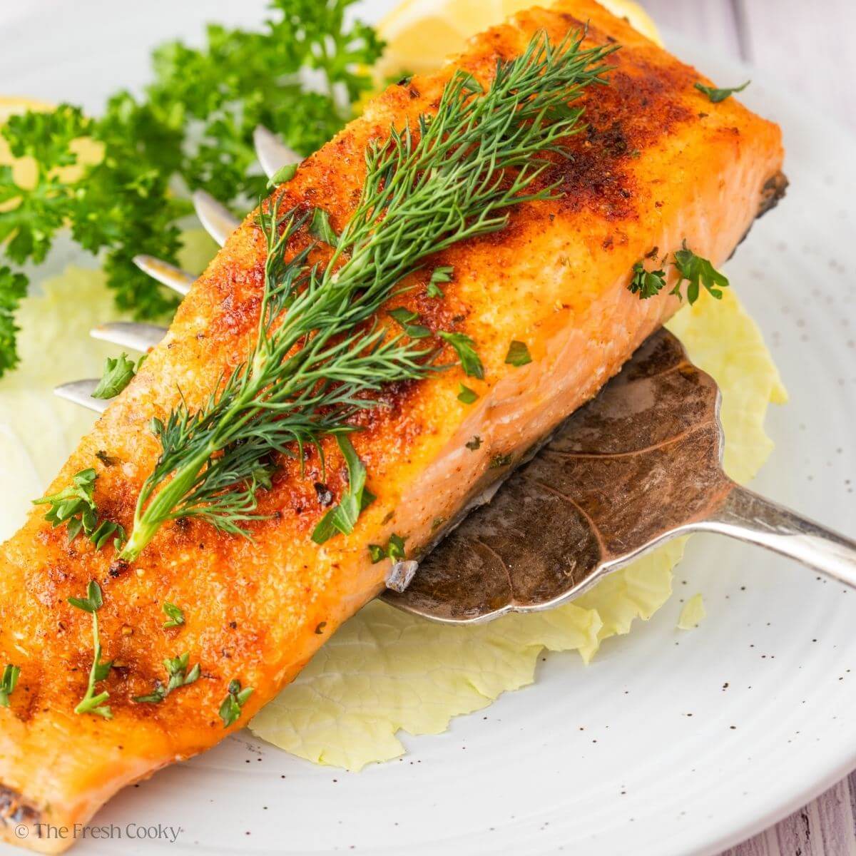 Using a serving fork to place the ai fryer salmon on a plate.