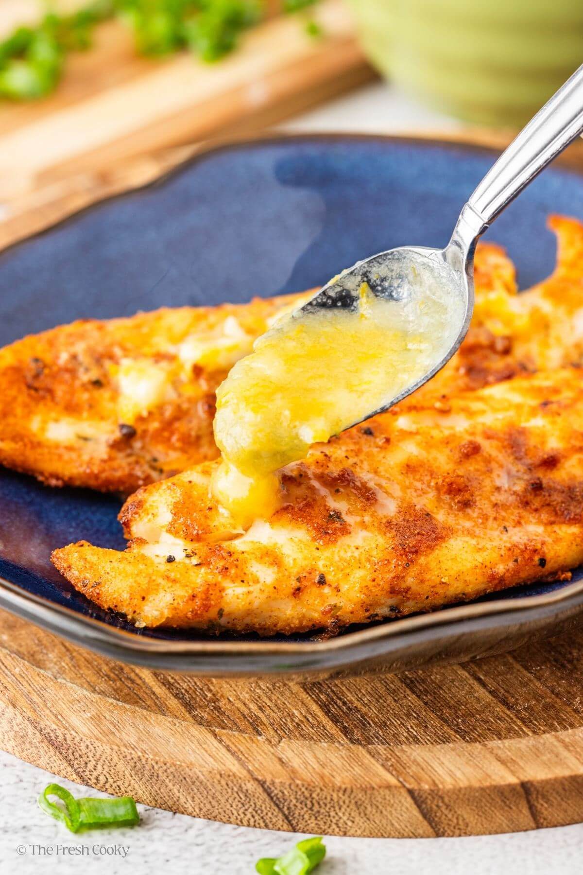 Spooling the lemon butter sauce over the top of the air fried tilapia on a plate.