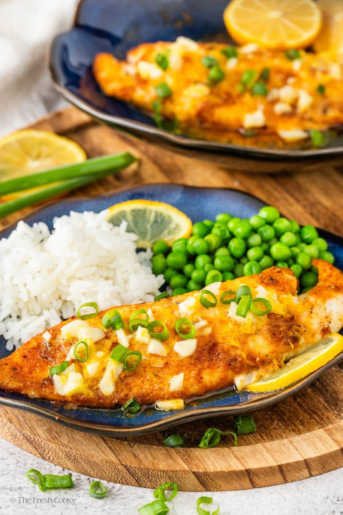Two plates of air fryer tilapia with one of them served with rice and peas on the side.