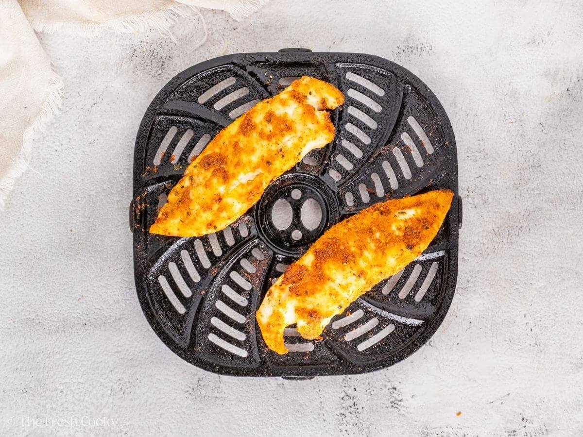 Tilapia fillets in the air fryer basket after being cooked.