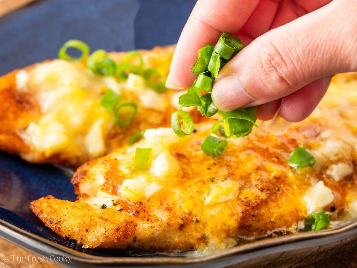 Hand sprinkling sliced green onions on top of the air fryer tilapia.