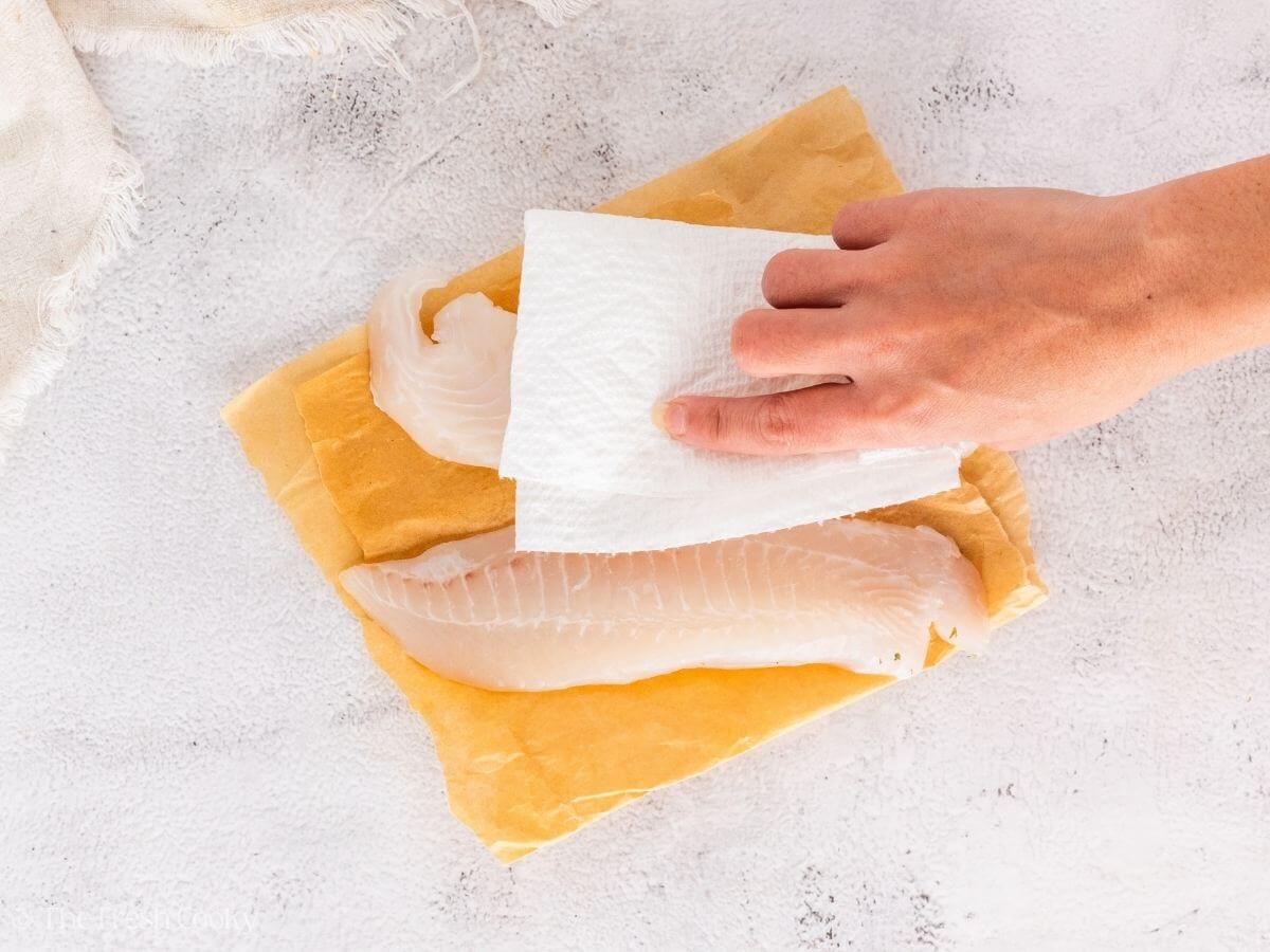 Patting dry the tilapia fillets with a paper towel.