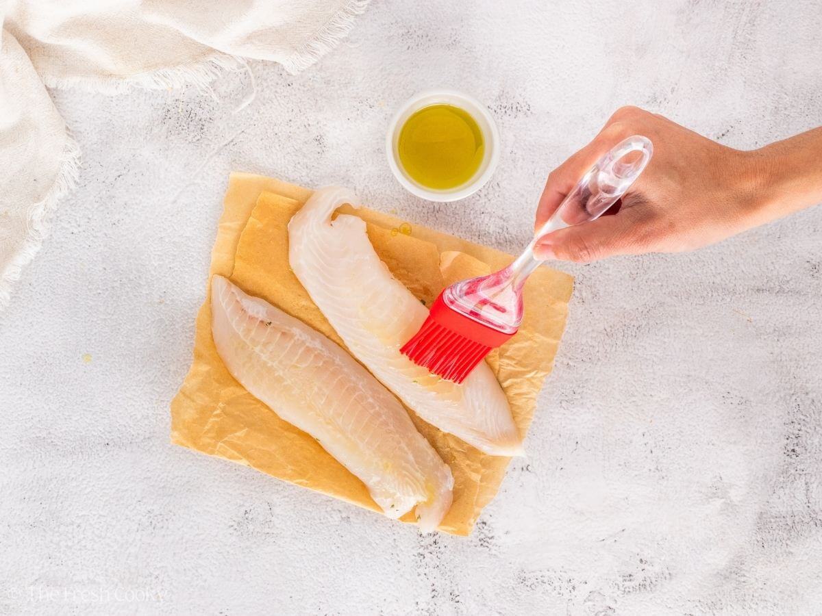 Brushing olive oil onto the tilapia fillets.
