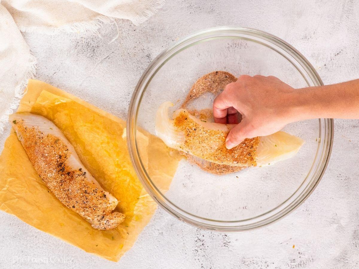 Pressing the tilapia into the seasoning in a bowl.