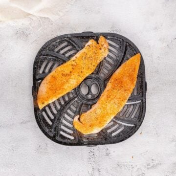 Placing the seasoned tilapia on the air fryer basket.