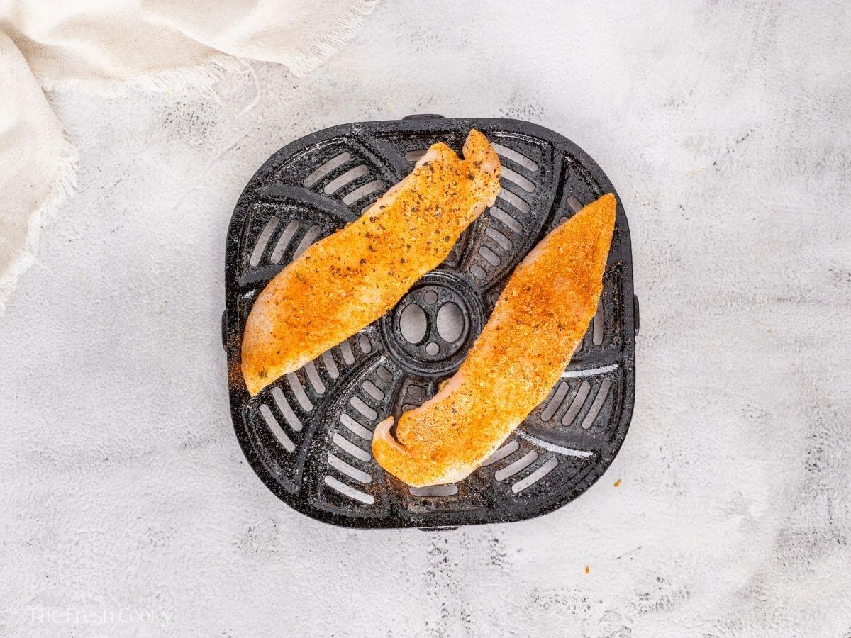 Placing the seasoned tilapia on the air fryer basket.
