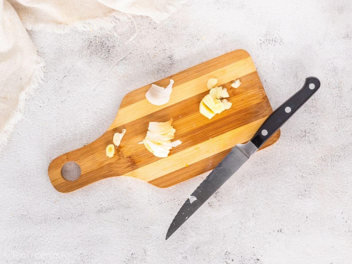 Diced garlic on a small wooden board with a knife.