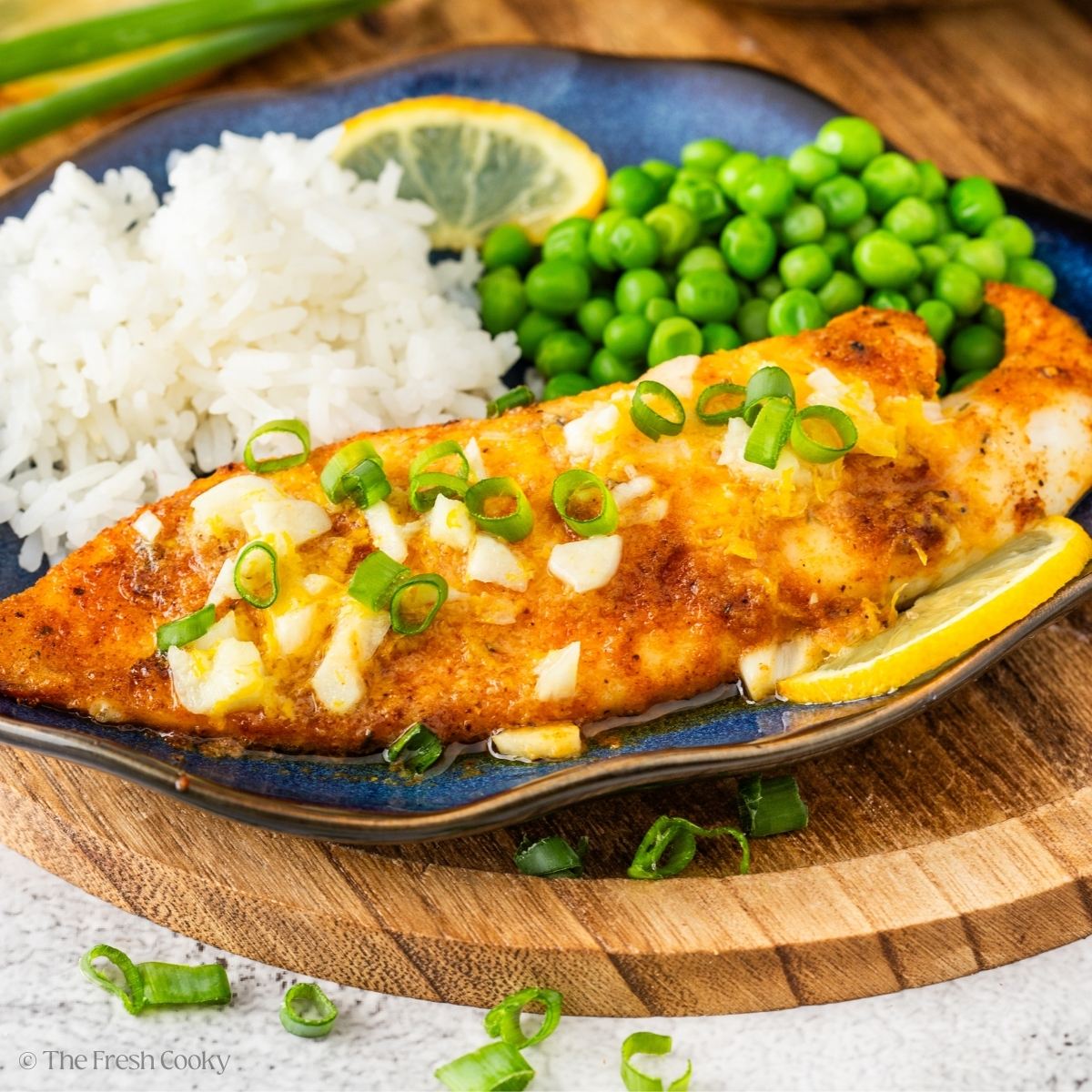 Air fried tilapia with lemon butter sauce, rice and peas on a plate.