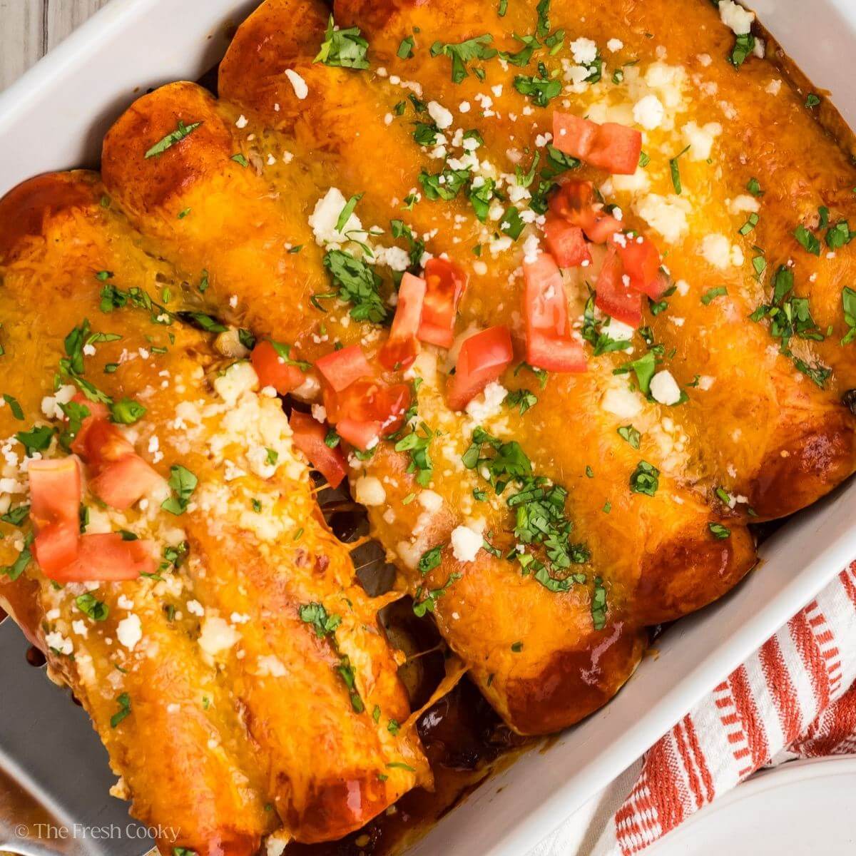 Baked chicken enchiladas in a white baking dish with a spatula taking some away.
