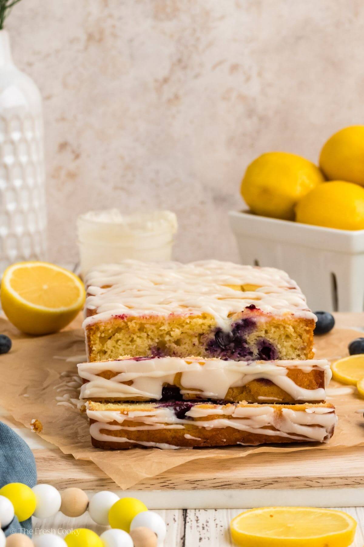Lemon blueberry bread on a wooden board lined with parchment with two slices off the end.
