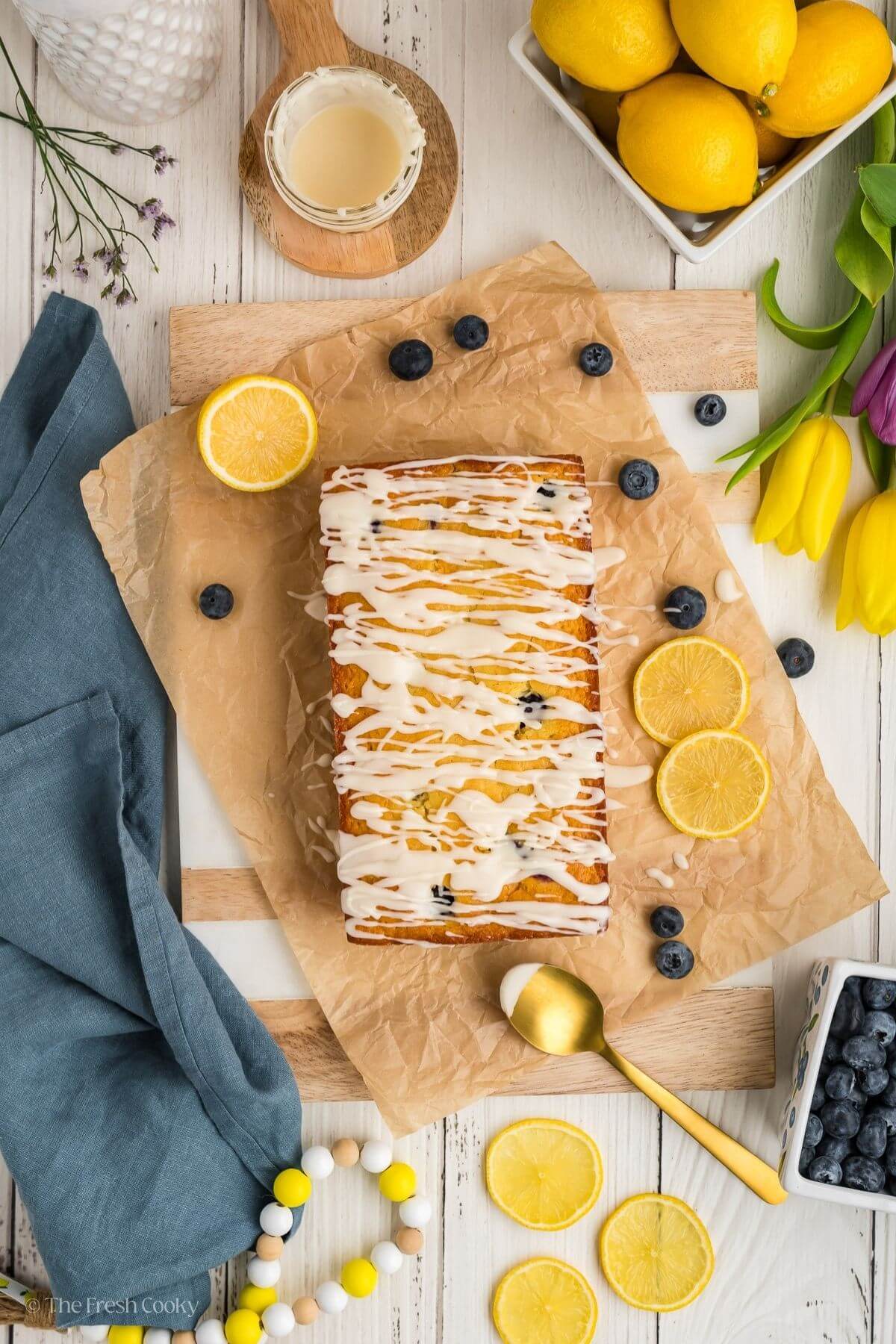Overhead shot of lemon blueberry bread with glaze on top surrounded by fresh lemon and blueberries.