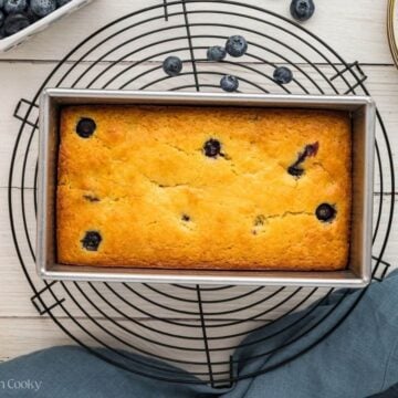Baked lemon blueberry loaf in the loaf pan on a cooling rack.