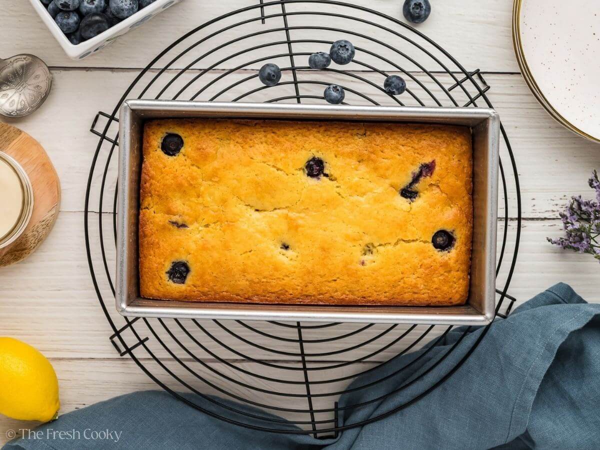 Baked lemon blueberry loaf in the loaf pan on a cooling rack.