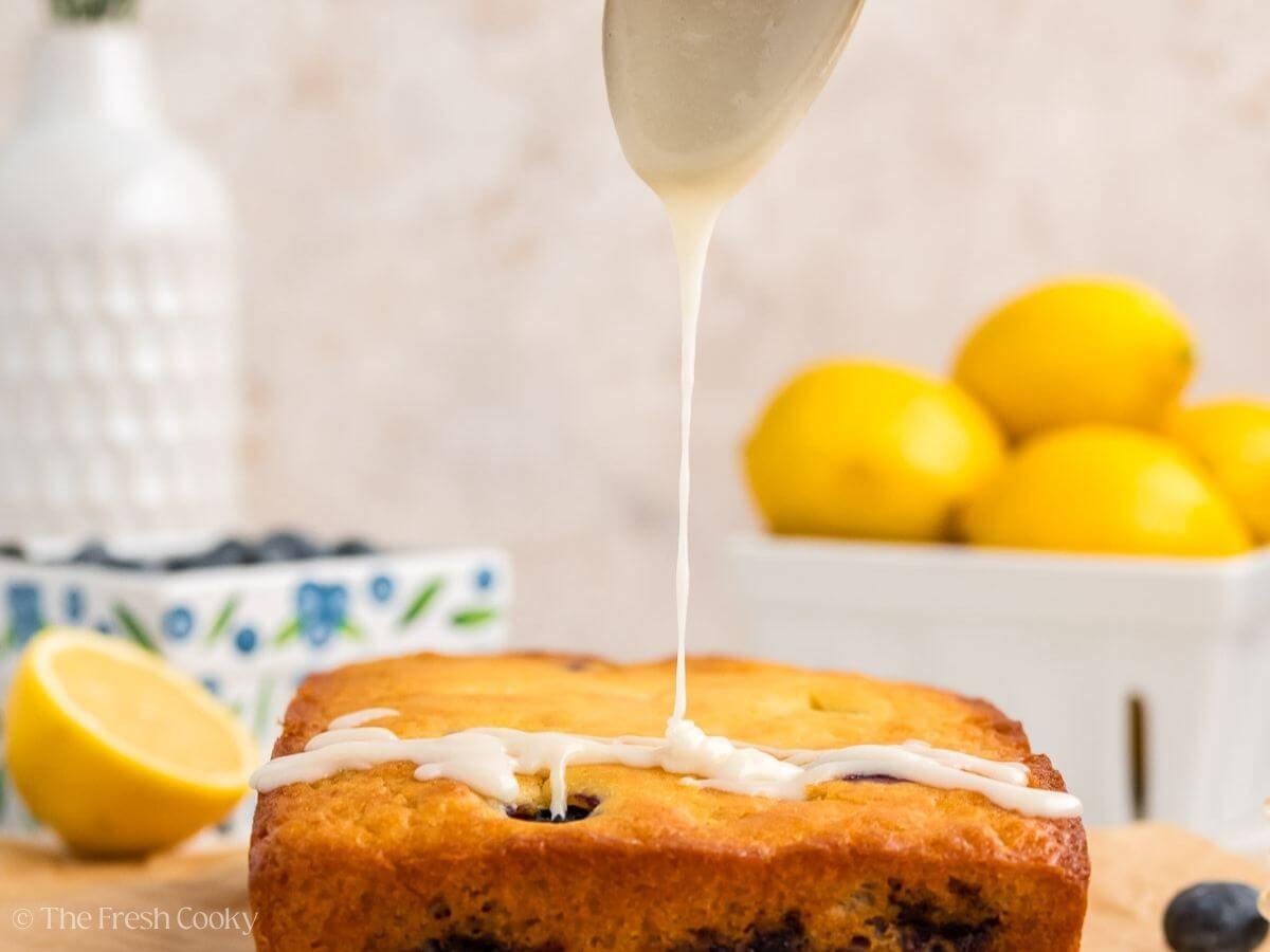 Spoon drizzling lemon glaze on top of the lemon blueberry bread.