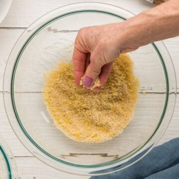 Hand rubbing sugar with lemon zest in a bowl.