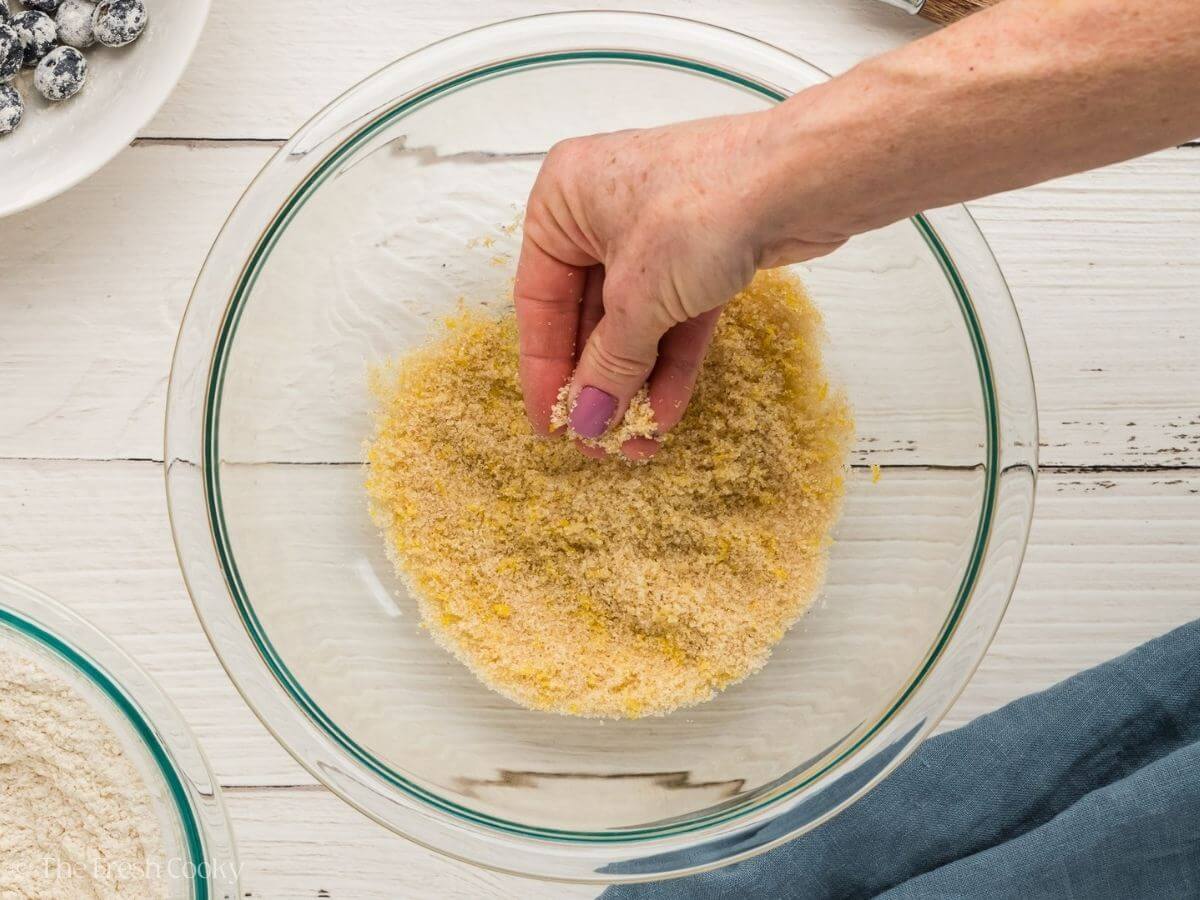 Hand rubbing sugar with lemon zest in a bowl.