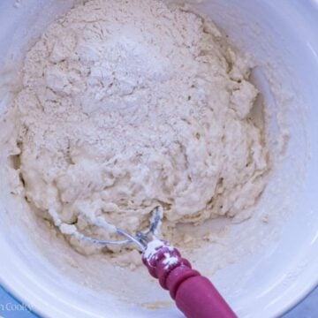 Using a dough whisk to combine the sourdough pizza dough in a mixing bowl.