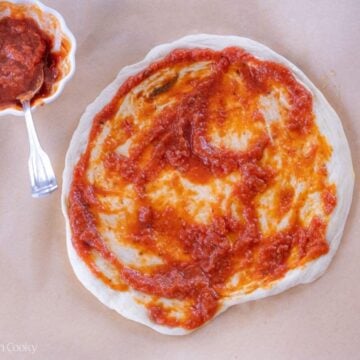 Overhead shot of sourdough pizza dough topped with red sauce.