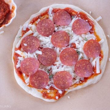 Pepperoni pizza on a piece of parchment paper before being baked.
