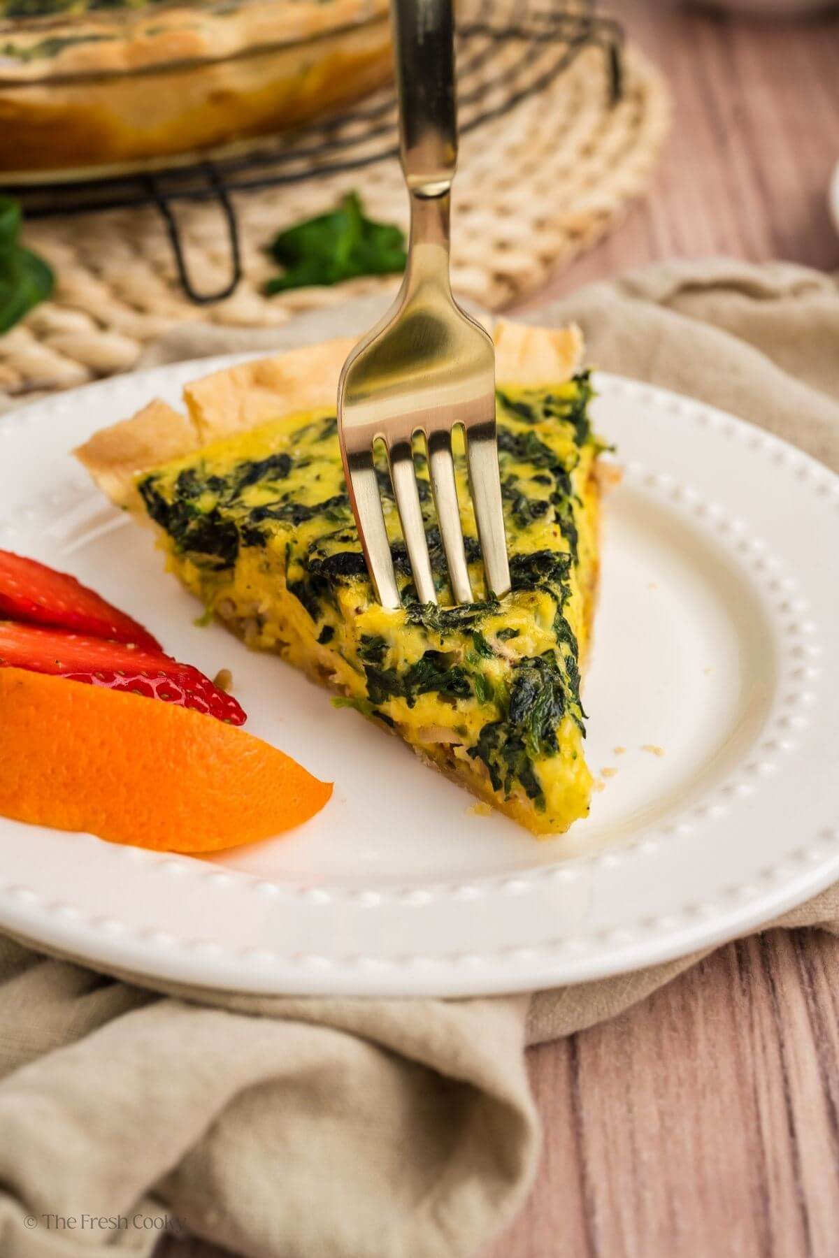 Slice of spinach quiche on a plate with a fork taking a bite.