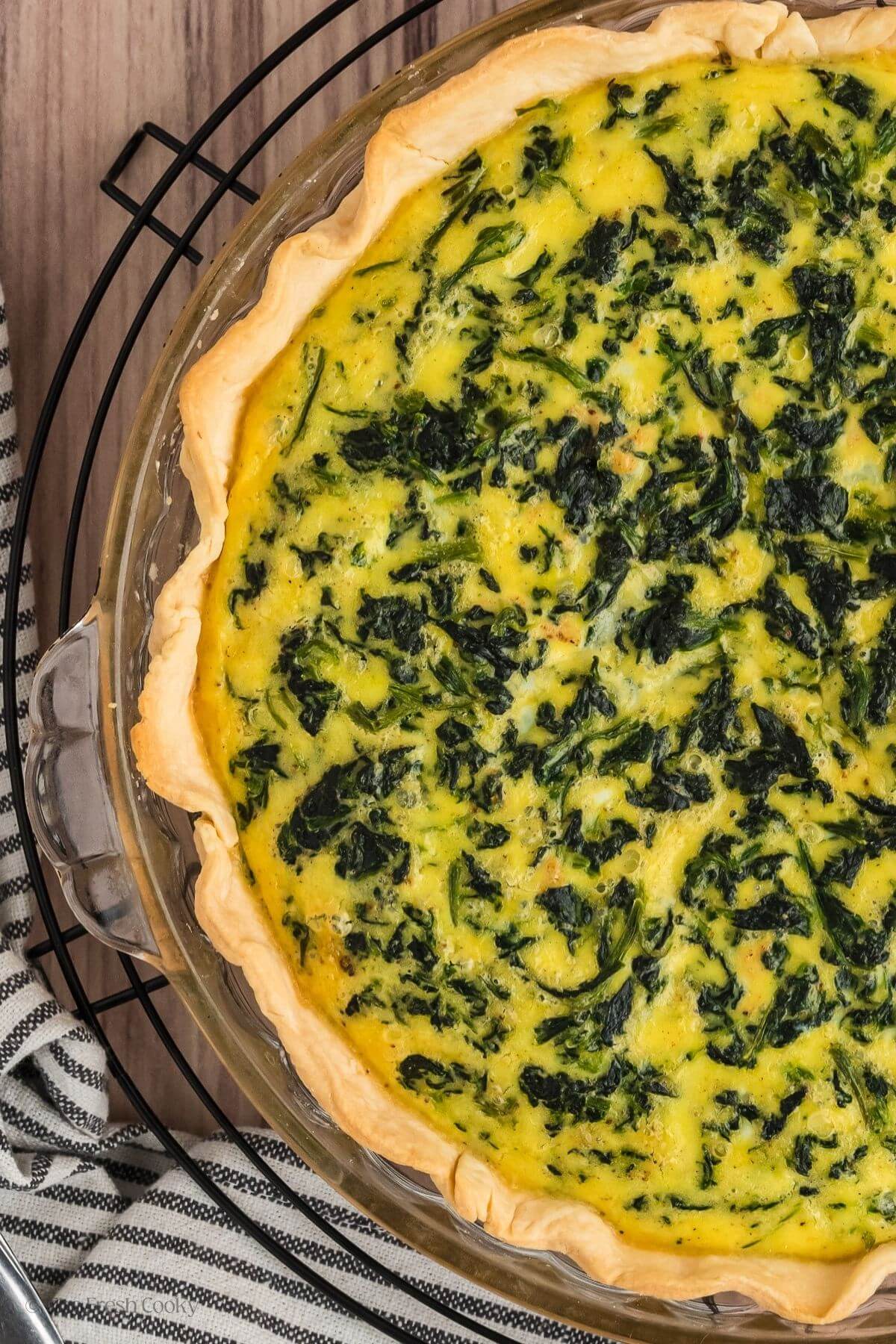 Overhead shot of half of the spinach quiche in the pie pan on a cooking rack.