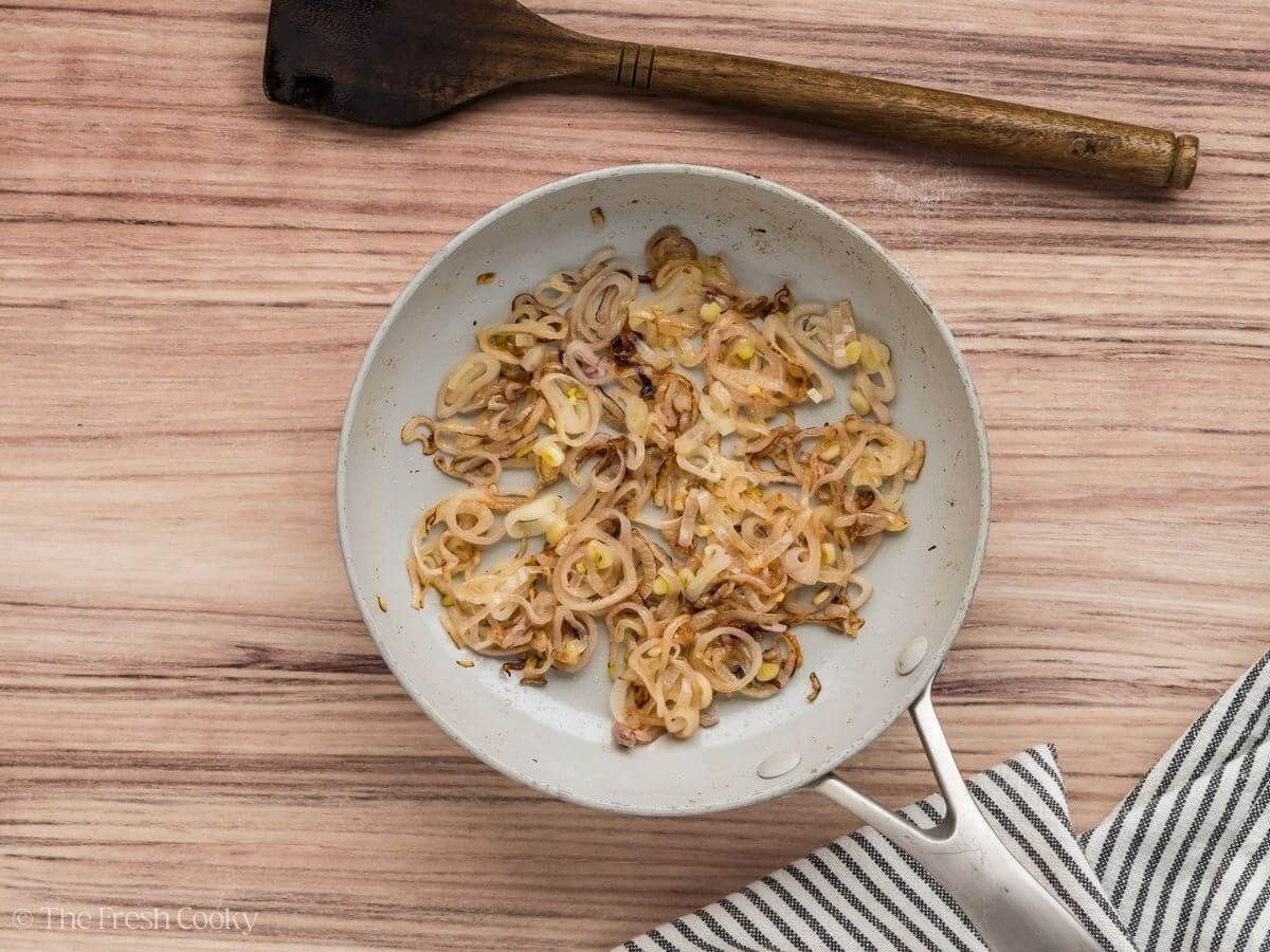 Sautéed sliced shallots in a skillet.