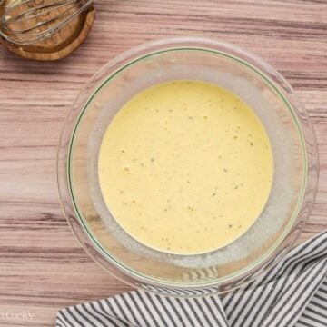 Eggs, cream and spices whisked together in a glass mixing bowl.