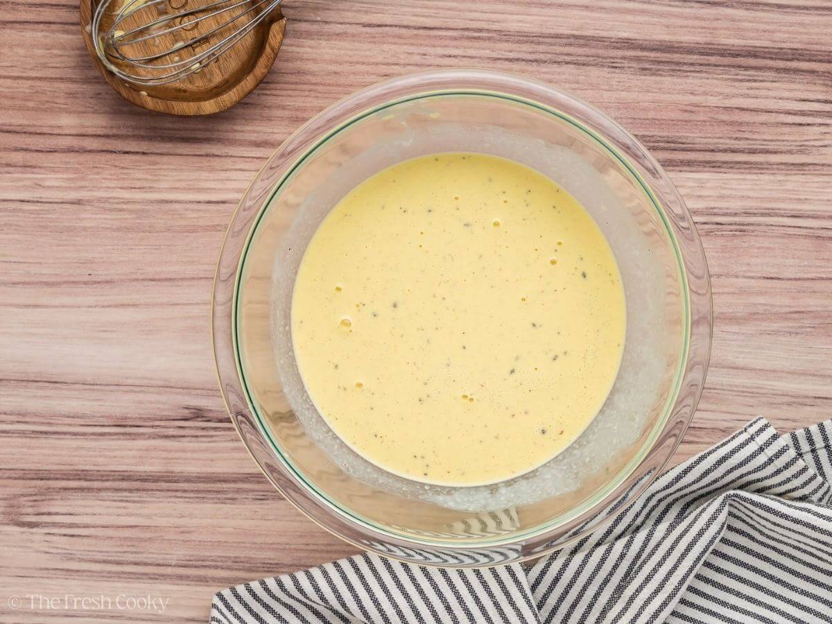 Eggs, cream and spices whisked together in a glass mixing bowl.
