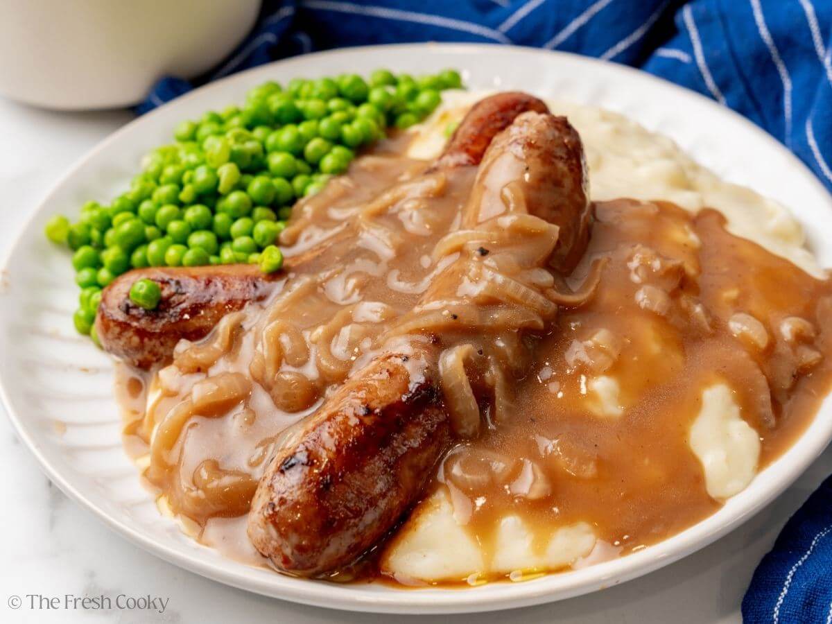 Plate filled with mashed potatoes and sausages smothered in onion gravy with peas. 
