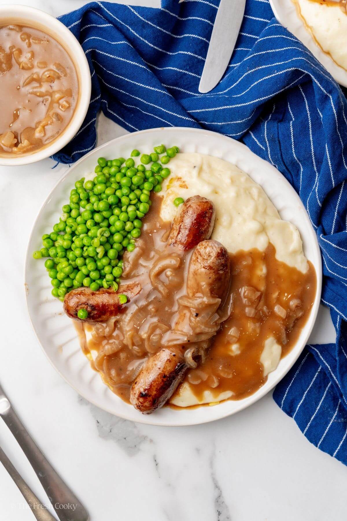 Top down shot of bangers and gravy over mashed potatoes with peas. 