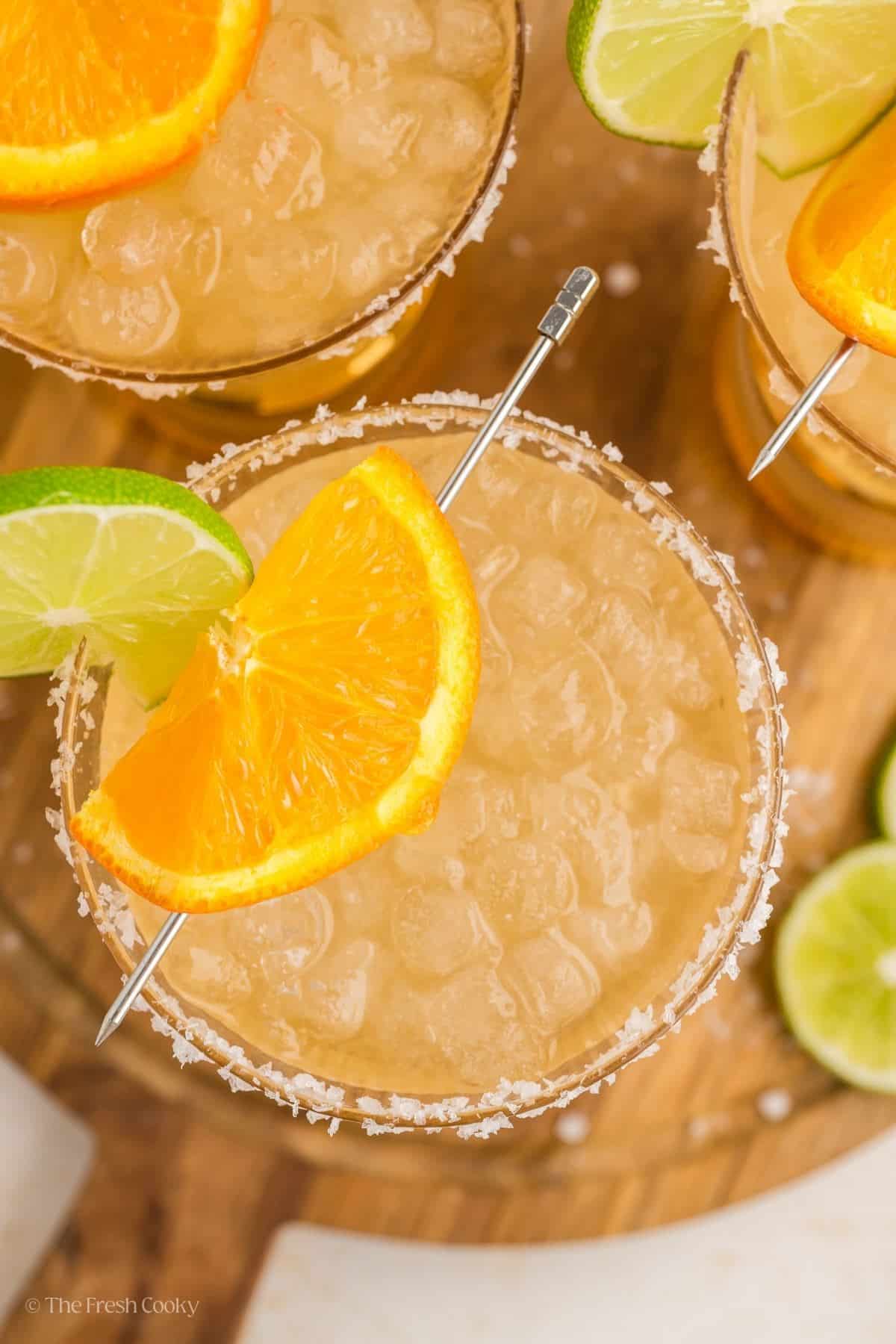 Looking down on a golden margarita garnished with orange and lime.
