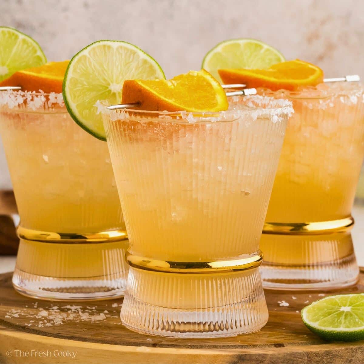 Three Cadillac margaritas with salted rims and orange garnish.