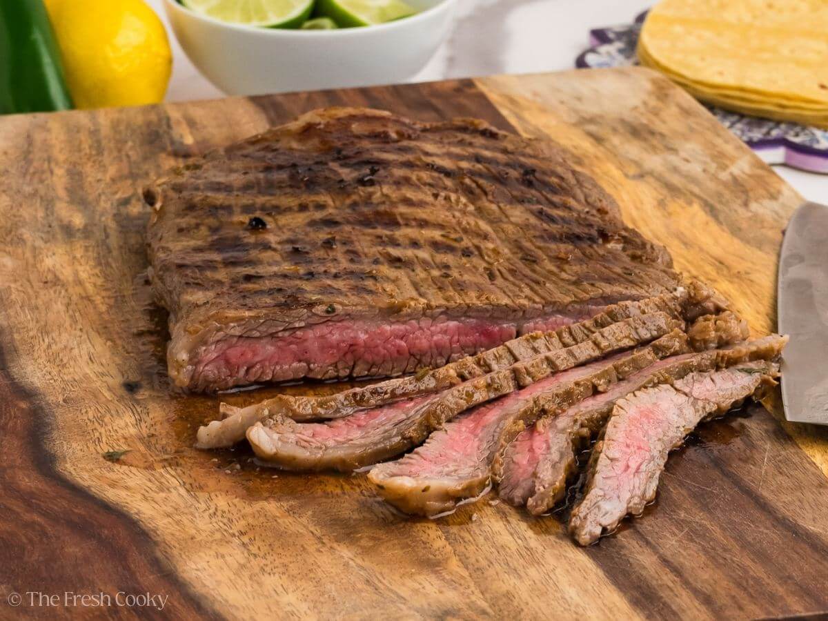 Carne asada on a wooden board with some slices of the meat off the end.