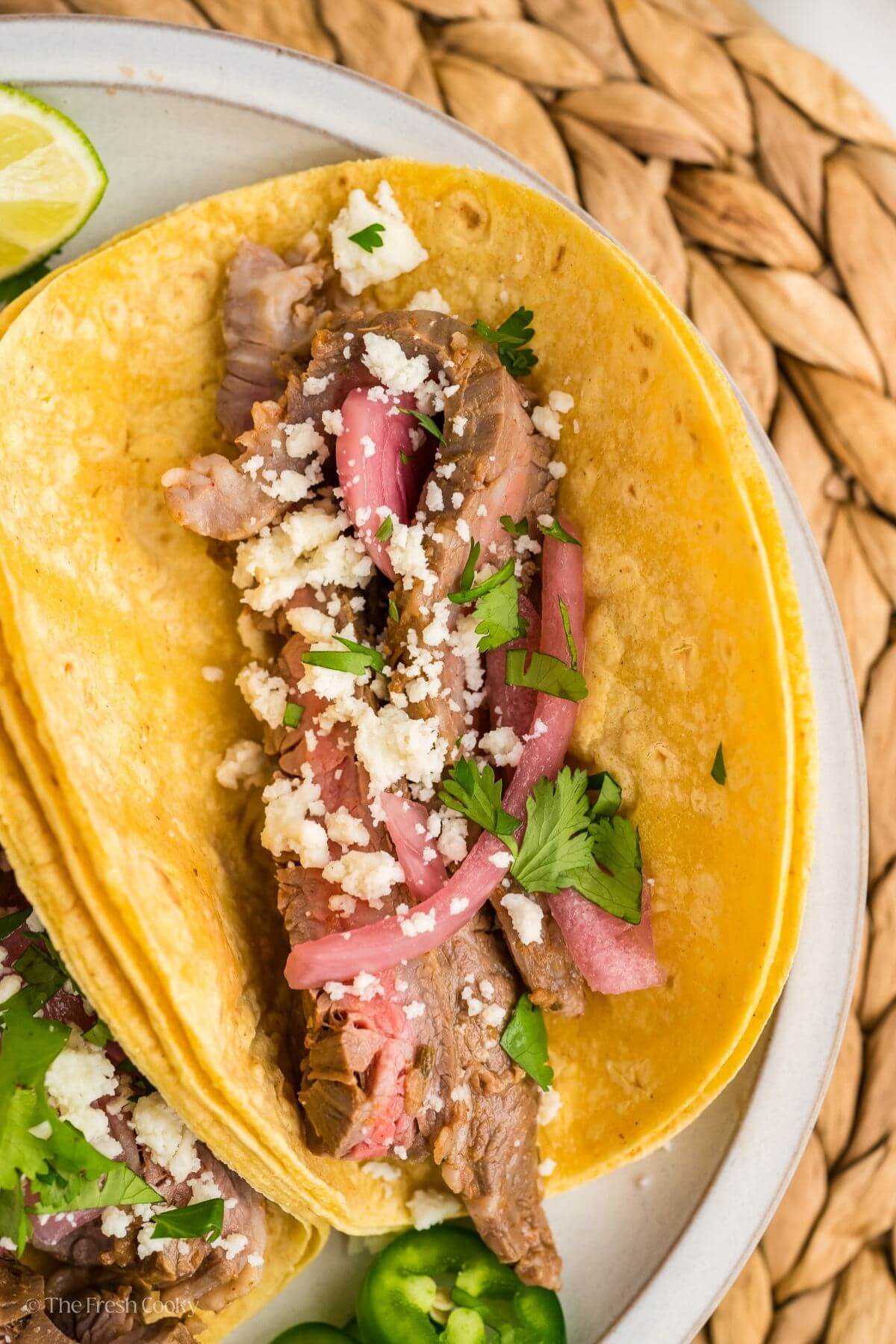 Overhead shot of carne asada on a corn tortilla topped with pickled onions and cotija cheese.